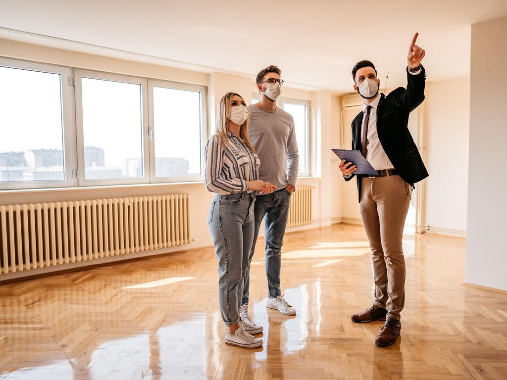 Pareja joven y agente masculino con máscaras faciales mientras buscan una nueva propiedad inmobiliaria